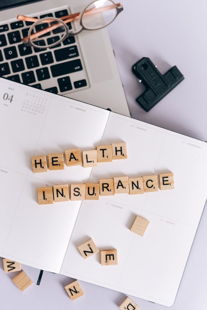 Words "Health Insurance" Made of Wooden Letter Tiles and Lying on a Calendar and Laptop